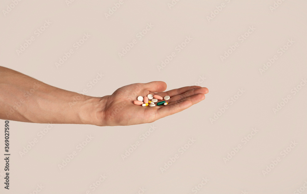 Unrecognizable young guy holding heap of pills in his hand over light background, closeup Unrecognizable young guy holding heap of pills in his hand over light background, closeup