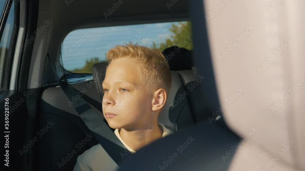 The concept of a family holiday. A school child sits in the back seat of a car and looks out the window enjoying the scenery of the trip. Pensive, dreaming child, sad at the window. The concept of a family holiday. A school child sits in the back seat of a car and looks out the window enjoying the scenery of the trip. Pensive, dreaming child, sad at the window.