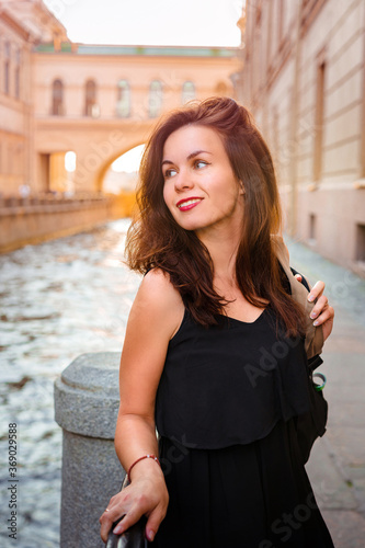 Vertical portrait of a young woman with long hair in a dress against the background of the canal in St. Petersburg on a summer day at sunset © KseniaJoyg