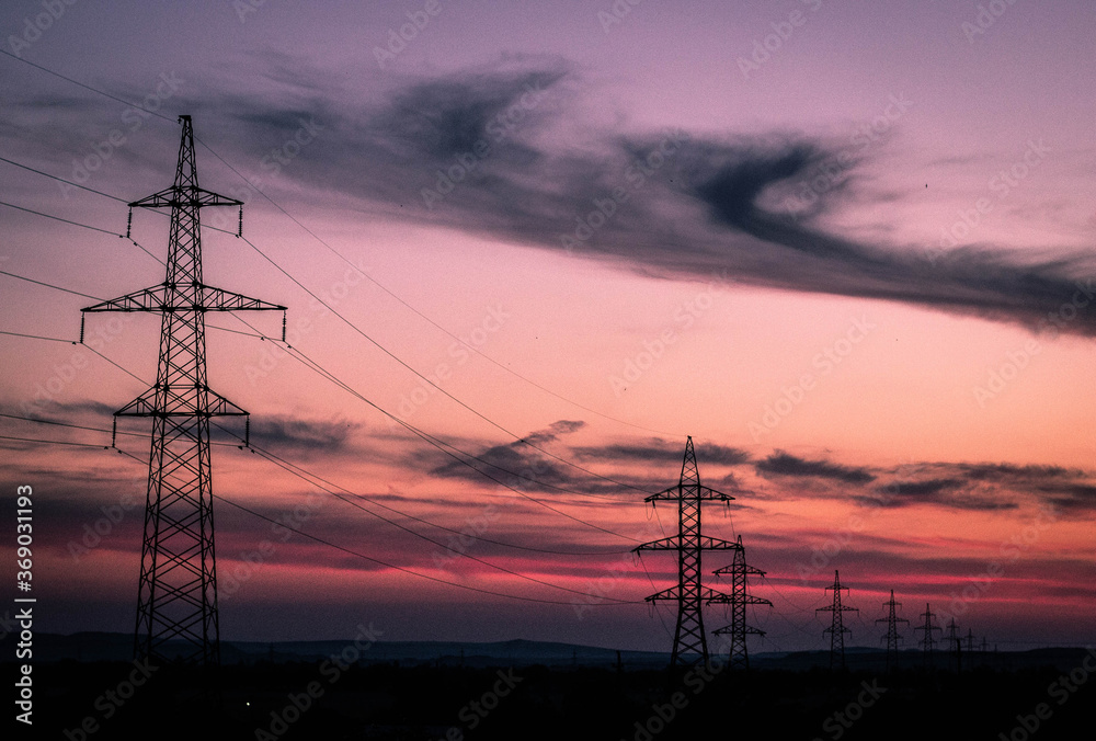 High voltage poles stand against the sunset