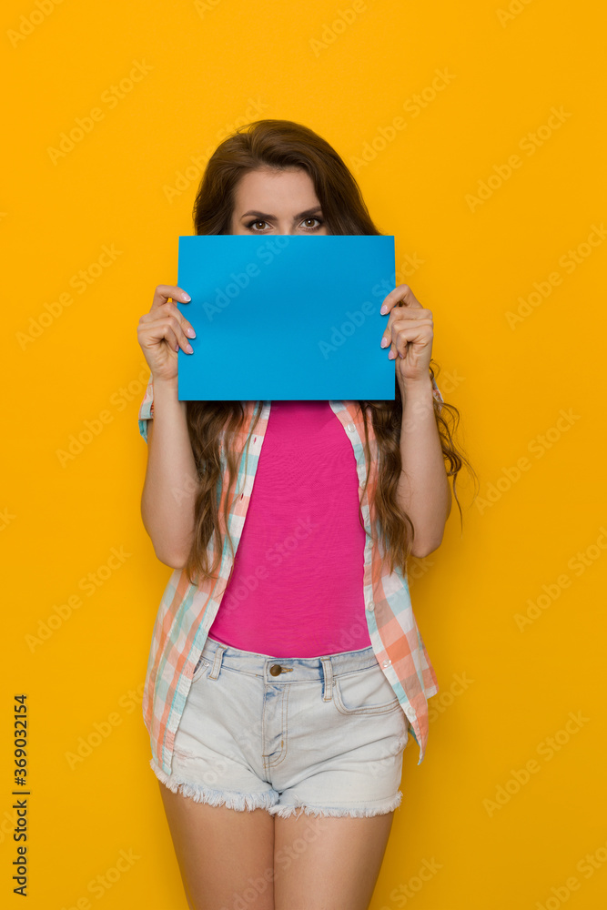 Young Woman Is Hiding Her Face Behind Blue Sheet Of Paper