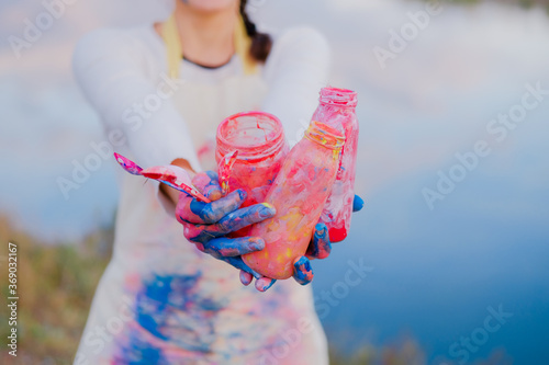 Girl in painted apron holding brushes and jar. Female artist outdoors