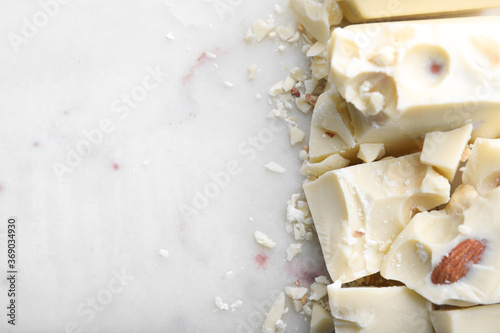 Pieces of white chocolate with nuts on light table  flat lay. Space for text