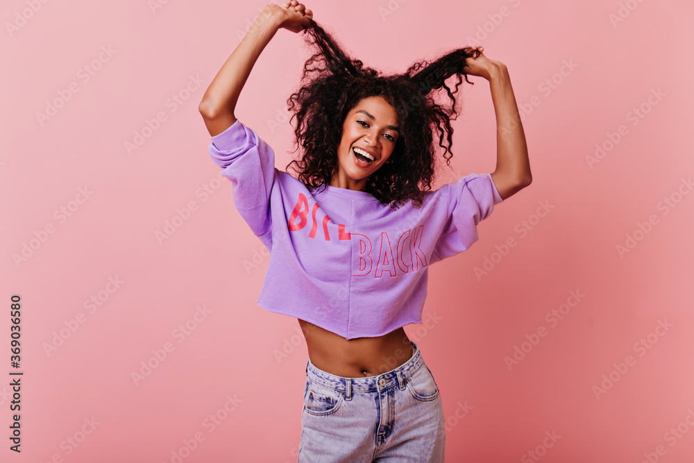 Sensual black girl posing on rosy background with happy face expression. Jocund african woman having fun in studio with pink interior. Sensual black girl posing on rosy background with happy face expression. Jocund african woman having fun in studio with pink interior.