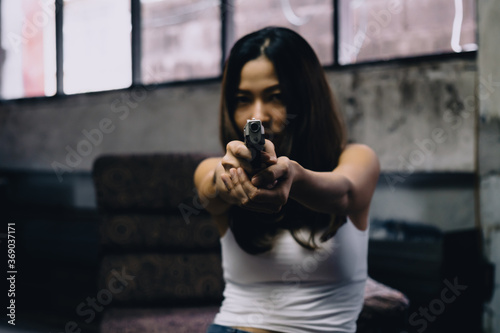 Asian woman holding a gun  aiming at the camera in abandon house  Illegal business concept