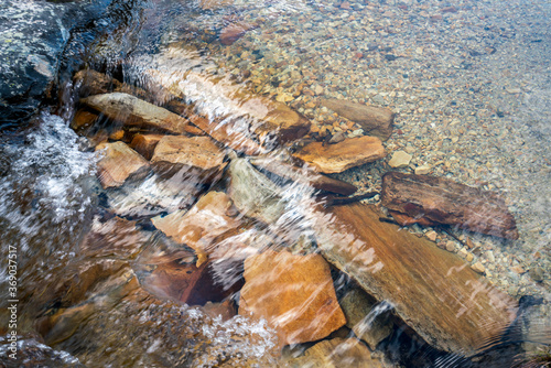 Little river with colorful stones during snow melting in spring.