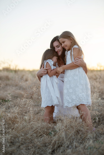 young mother with daughters posing and hugging for a photo at sunset in the field