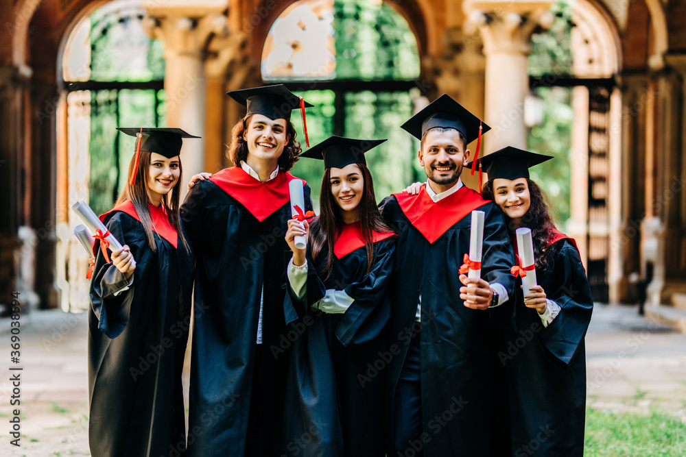 Obraz premium Happy graduation day. 5 graduates hold his graduate diplomas in their hands.