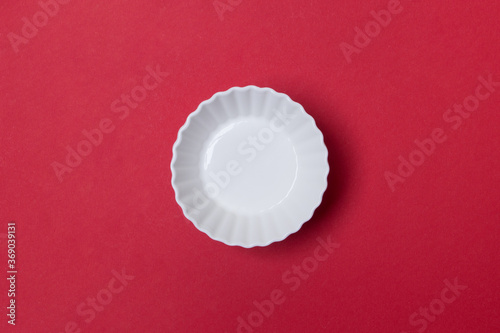 empty white plate on red colored paper background