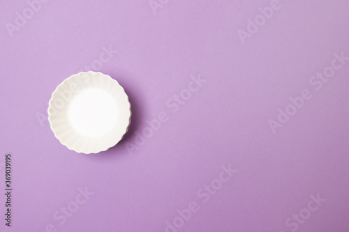empty white plate on purple colored paper background with copy space
