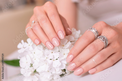 Close up view of beautiful female hands with romantic wedding manicure nails  nude gel polish and white flowers