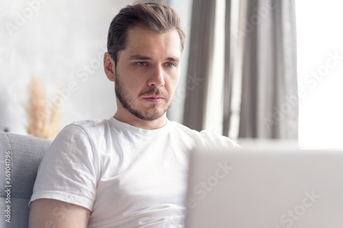 Typing new blog post. Handsome young man using his laptop with smile while sitting on the couch at home