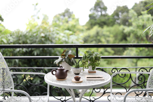 teapot and cup with small plants in white pots with notebook on white metal table at balcony outdoor