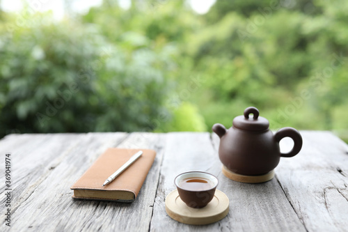 Brown traditional teapot and cup with orange leather book on rustic grey wooden table