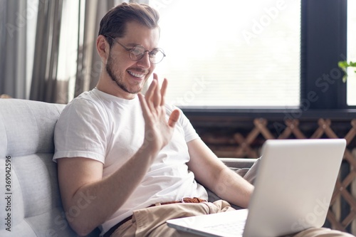Happy young man video chatting on laptop computer while sitting on the sofa at home