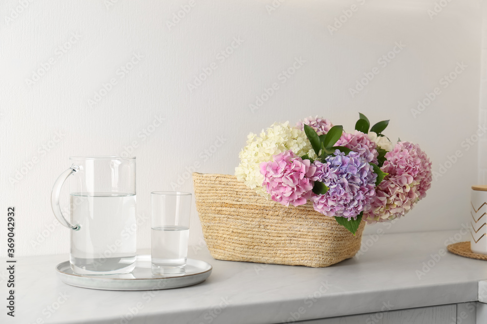 Beautiful hydrangea flowers in basket and water on light table