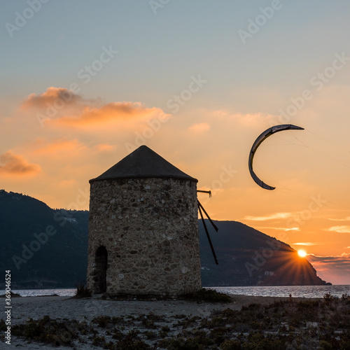 Kitesurfer silhouetted against the sunset by ann old windmill on Gyra beach Lefkada