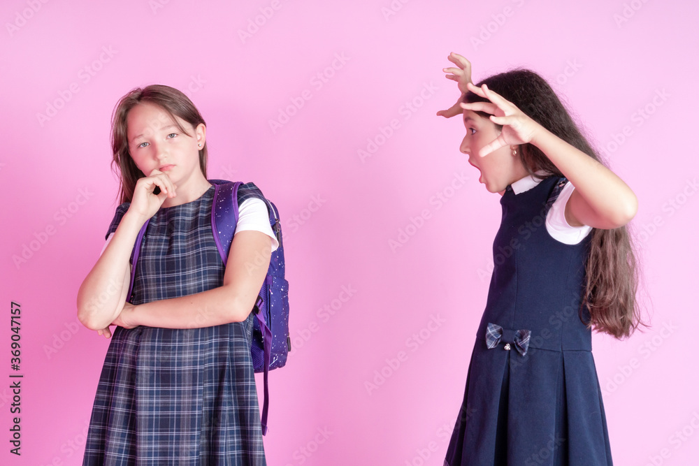 Two schoolgirls are quarreling on a pink background. One girl does not react to another girl's aggression. Concept of the day International day of non violence. Two schoolgirls are quarreling on a pink background. One girl does not react to another girl's aggression. Concept of the day International day of non violence.