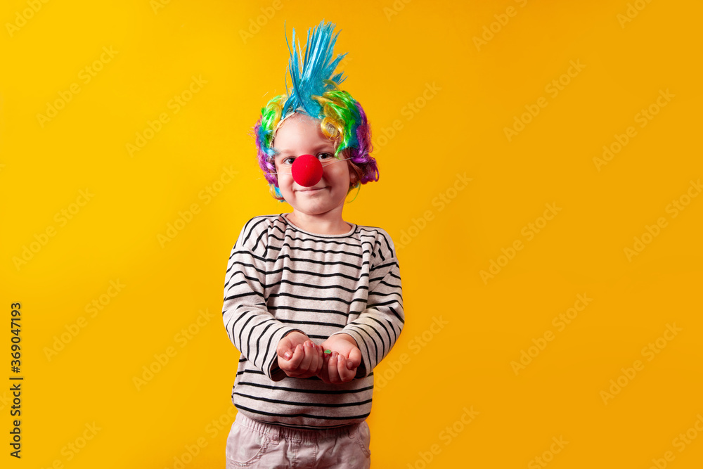 A girl in a wig and red nose stands on a yellow background in the studio, the concept of the holiday A girl in a wig and red nose stands on a yellow background in the studio, the concept of the holiday