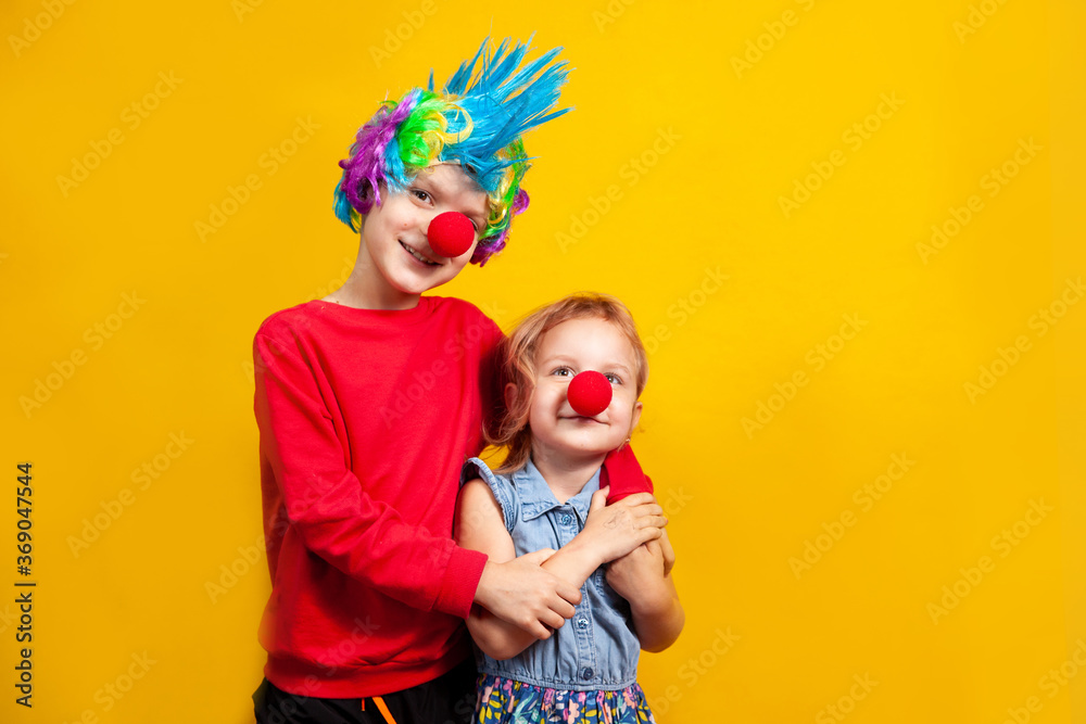 boy in a clown costume, a wig and a bright nose, the concept of a holiday and fun on a yellow background in the studio, a portrait to the waist boy in a clown costume, a wig and a bright nose, the concept of a holiday and fun on a yellow background in the studio, a portrait to the waist