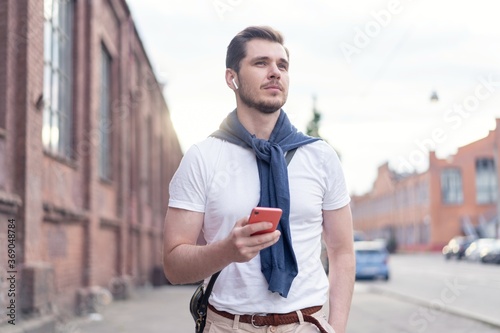 Handsome smiling man listening to music while walking in the city.