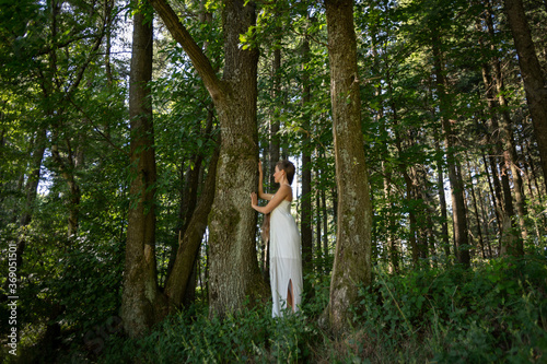 Frau steht in weißem Kleid im Wald, Waldbaden in der Natur, Erholung vom Alltags Stress.