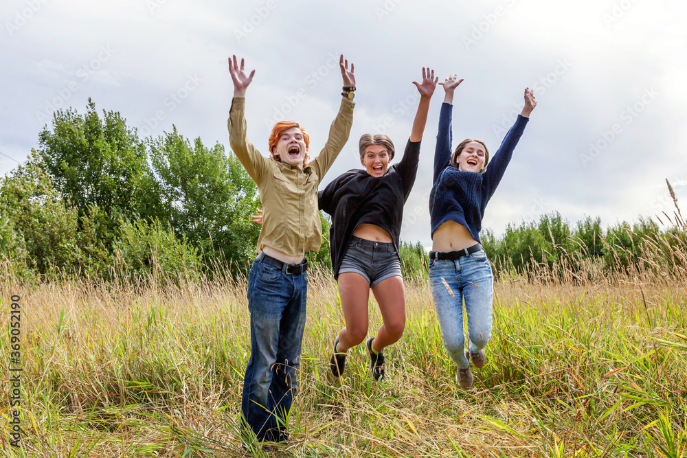 Summer holidays vacation happy people concept. Group of three friends boy and two girls jumping, dancing and having fun together outdoors. Picnic with friends on road trip in nature Summer holidays vacation happy people concept. Group of three friends boy and two girls jumping, dancing and having fun together outdoors. Picnic with friends on road trip in nature