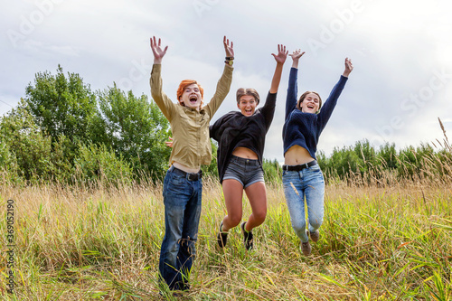 Summer holidays vacation happy people concept. Group of three friends boy and two girls jumping, dancing and having fun together outdoors. Picnic with friends on road trip in nature
