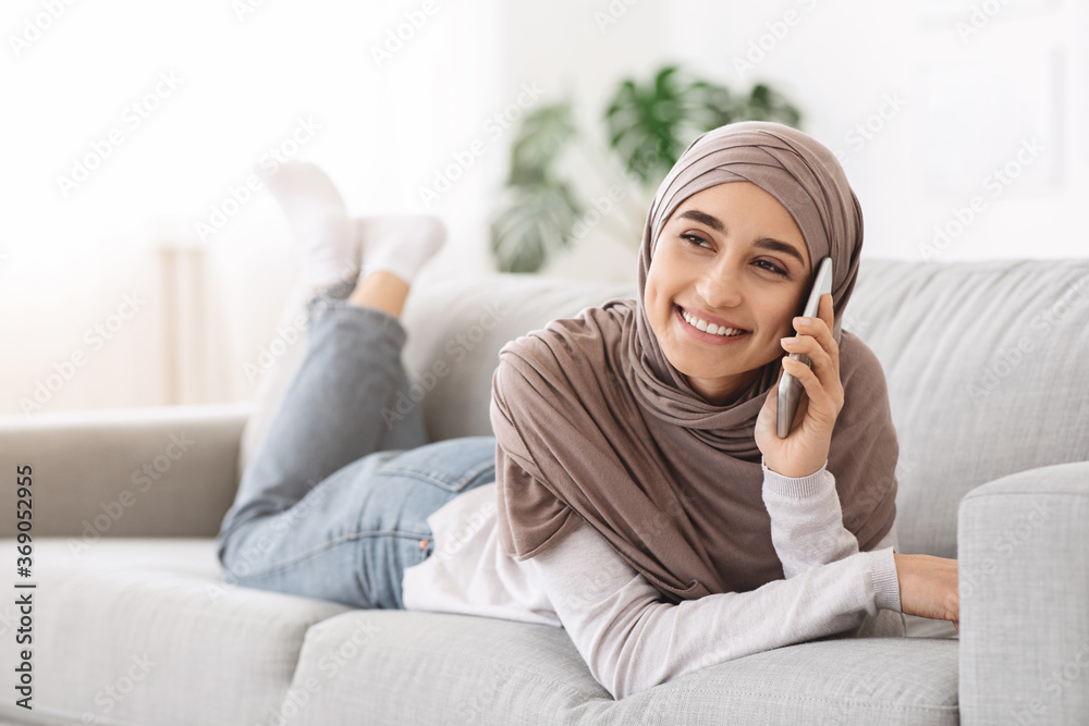 Smiling Arabic Girl Relaxing On Couch At Home, Talking On Cellphone Smiling Arabic Girl Relaxing On Couch At Home, Talking On Cellphone