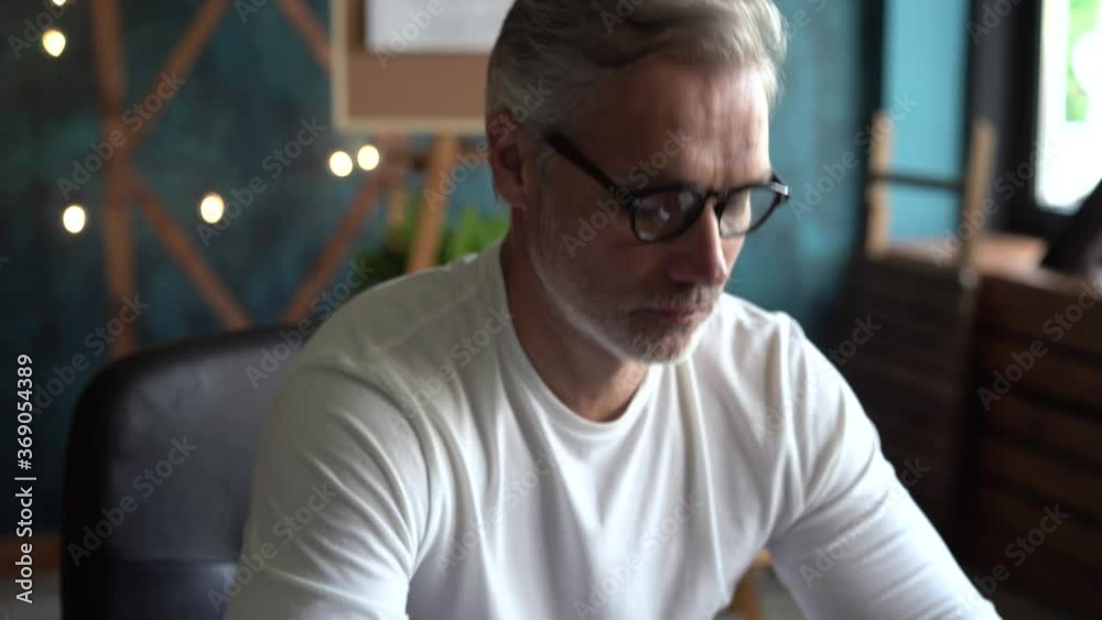 Senior freelancer using computer working from office. Smiling grey-haired man in glasses typing on computer. Senior freelancer using computer working from office. Smiling grey-haired man in glasses typing on computer.