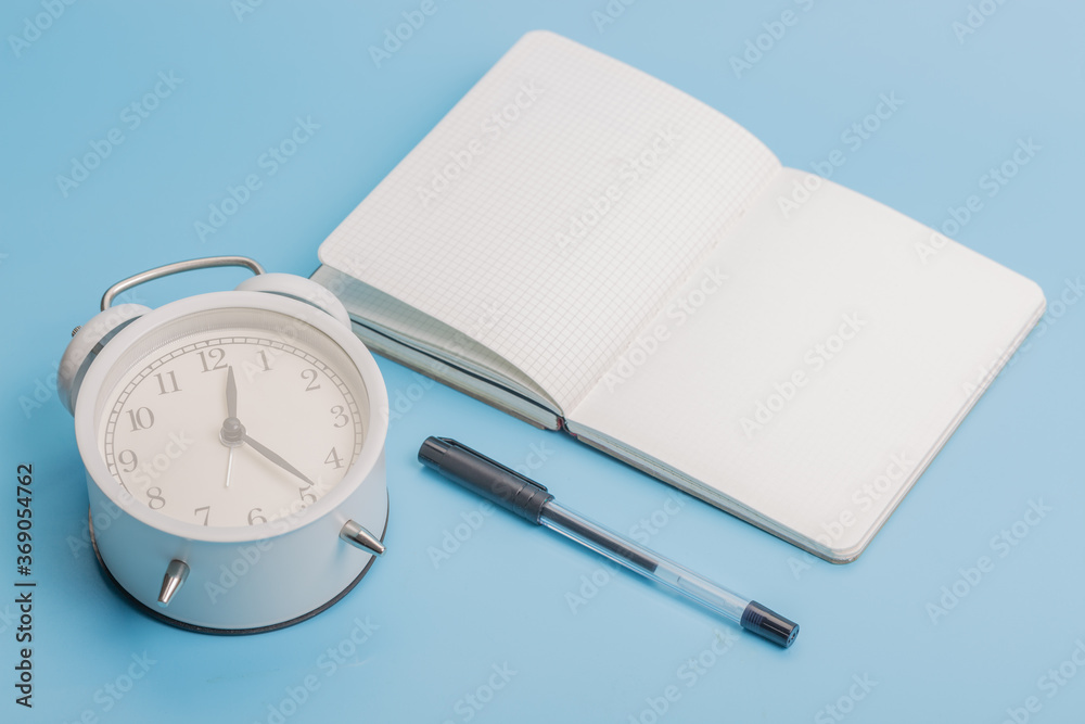 Notebook alarm clock pen on blue background Notebook alarm clock pen on blue background