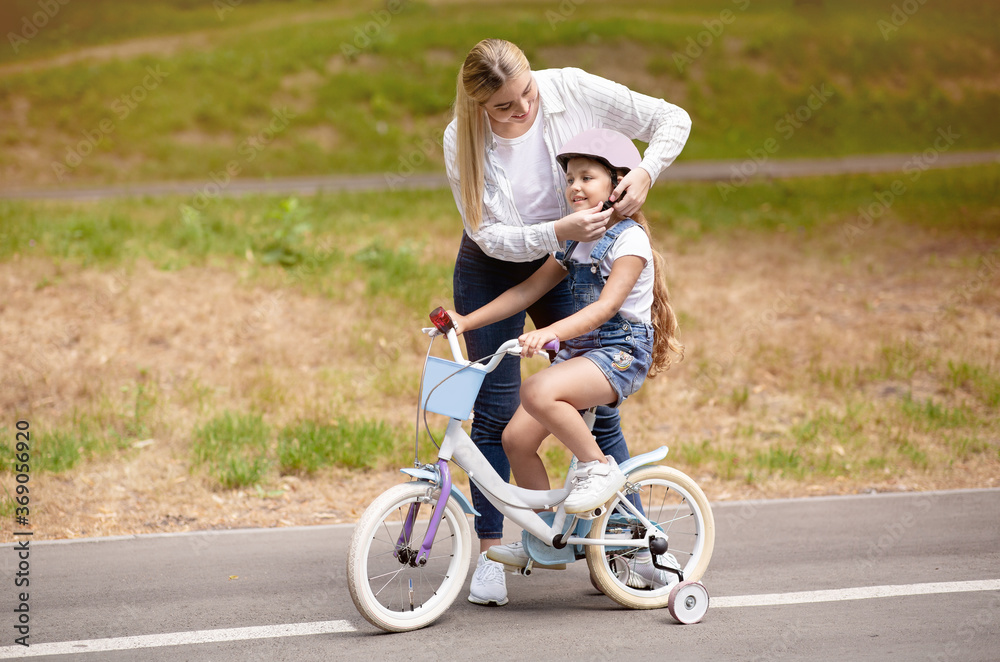 Mother Teaching Daughter To Ride Bike With Stabilisers Outside Mother Teaching Daughter To Ride Bike With Stabilisers Outside