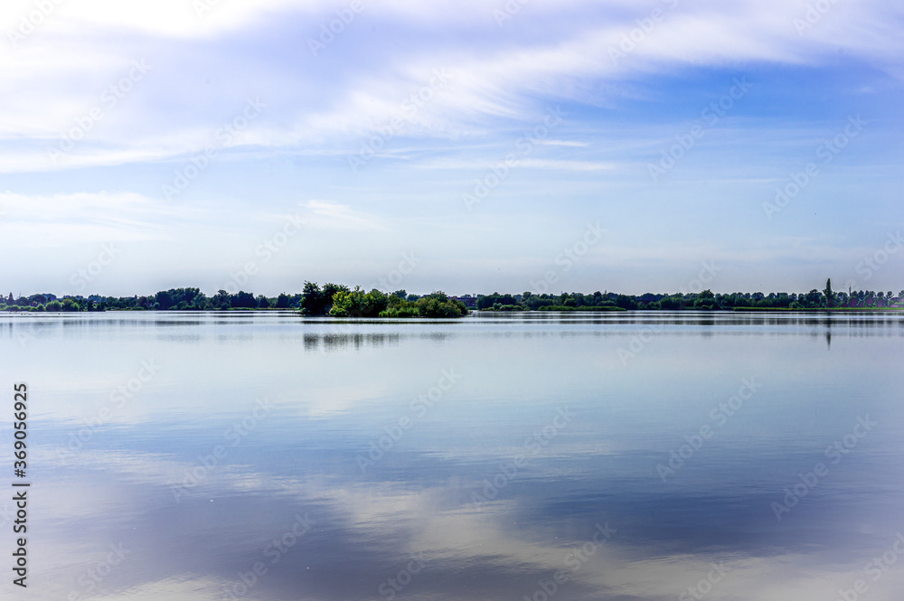 Quiet landscape of a lake in Reeuwijk. The rippling water reflects the fanned out clouds in the sky. South Holland, The Netherlands, Europe.