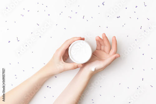 Beautiful well-conditioned female hands moisturizing cream surrounded with lavender flowers on the white background. Hand and body care concept