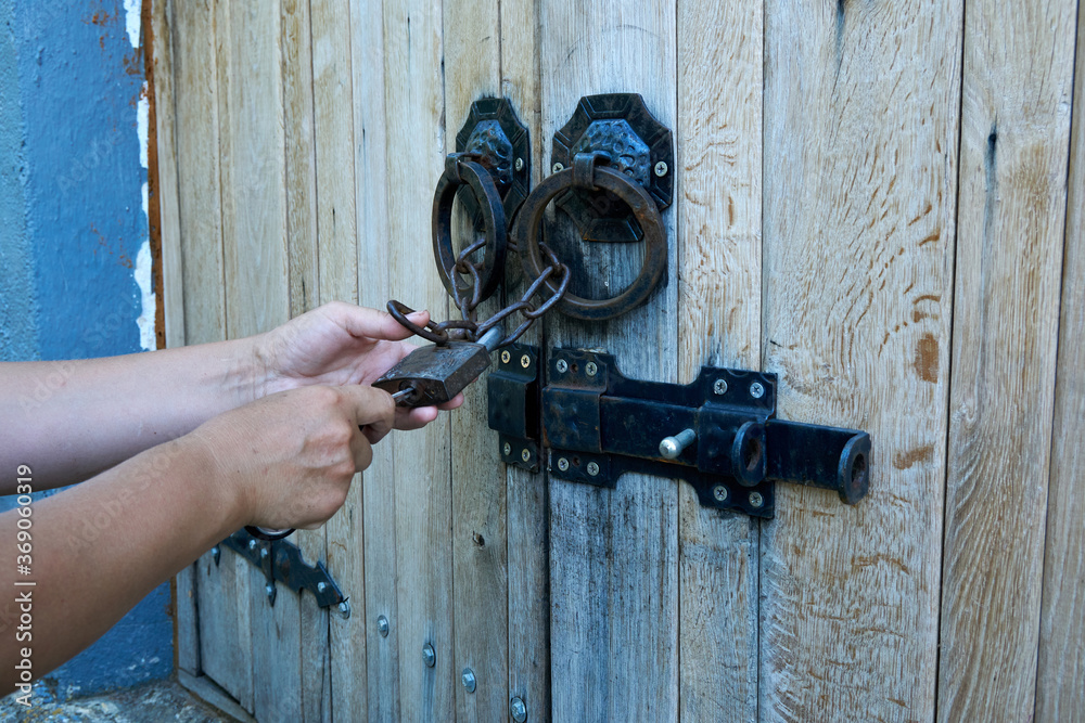 Women opens an ancient wooden door decorated with wrought iron elements. Old lock with an iron handle. Close-up. Selective focus. Women opens an ancient wooden door decorated with wrought iron elements. Old lock with an iron handle. Close-up. Selective focus.