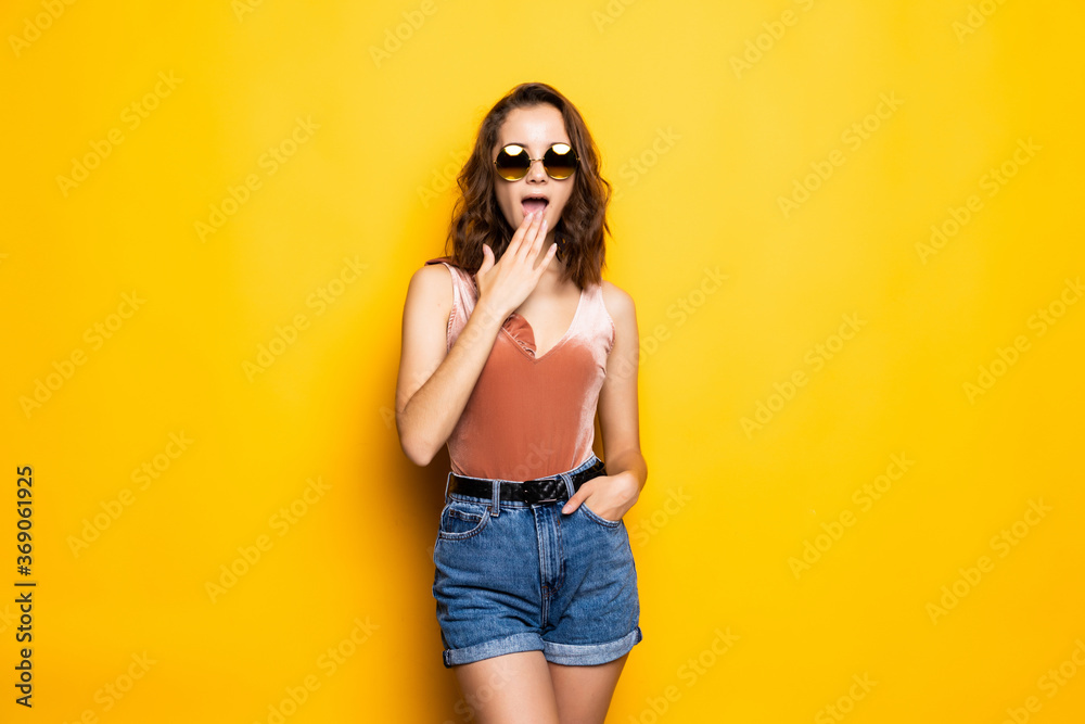 Shocked surprised girl in sunglasses and a summer hat, on a yellow background. Travel, vacation, summer