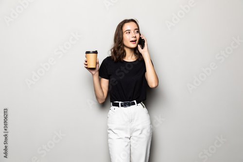 Young business woman talking by mobile phone drinking coffee posing isolated over grey background