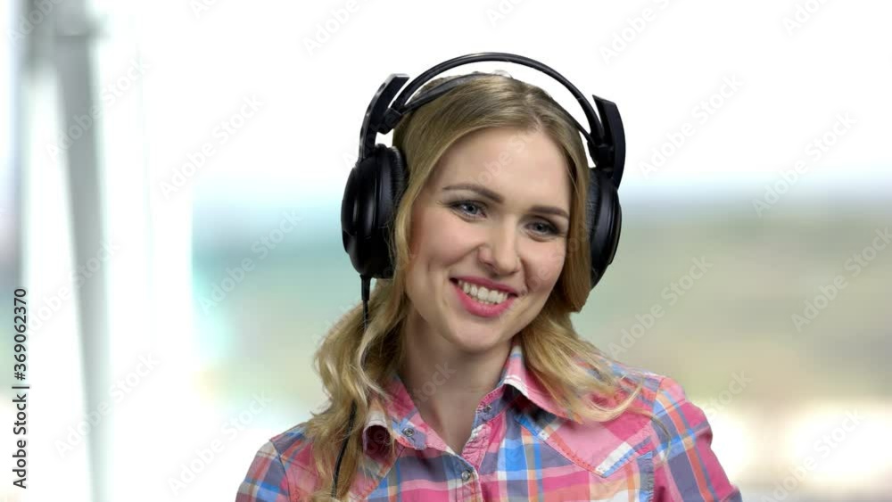 Close up young happy woman using headphones. Girl wearing headphones and talking while having a call. Abstract blurred background. Close up young happy woman using headphones. Girl wearing headphones and talking while having a call. Abstract blurred background.
