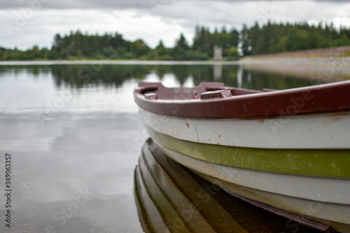 A close up view of a wooden row boat on a calm still lake shore