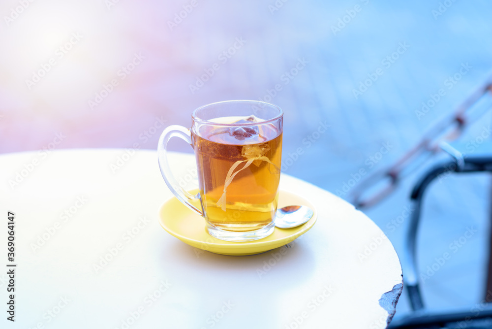 Tea on white table sea port background ,warm tone. Tea bags in glass on a restaurant in the port near the sea lit by the setting sun. Concept of vacation, relaxation, calm, lifestyle. Tea on white table sea port background ,warm tone. Tea bags in glass on a restaurant in the port near the sea lit by the setting sun. Concept of vacation, relaxation, calm, lifestyle.