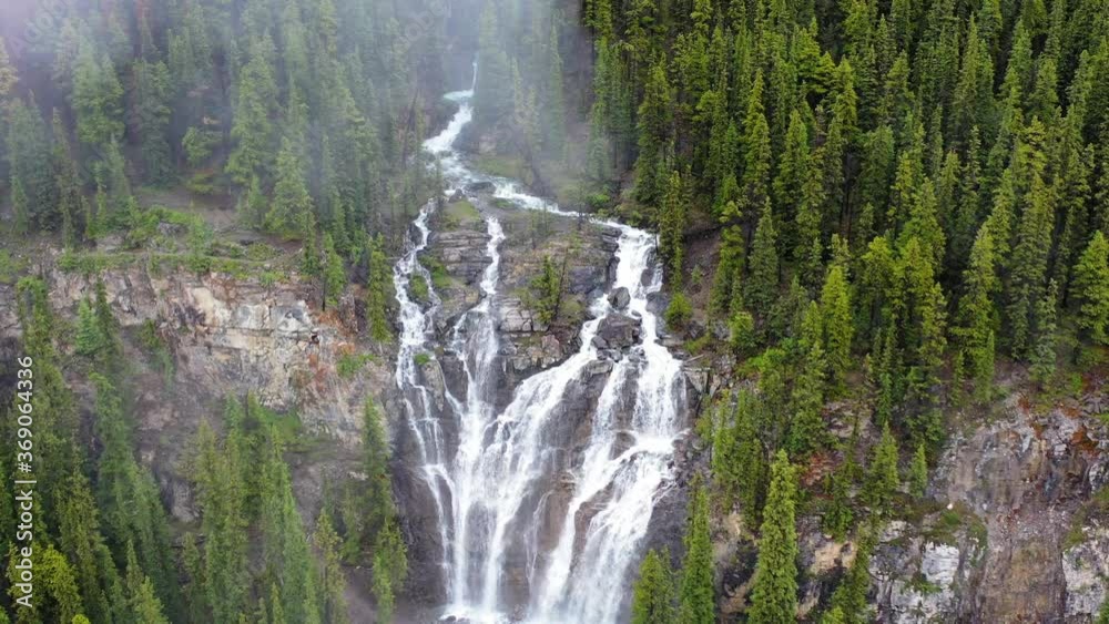 Aerial shot of rushing waterfall surrounded by thick forest, slowly tilting down. Aerial shot of rushing waterfall surrounded by thick forest, slowly tilting down.