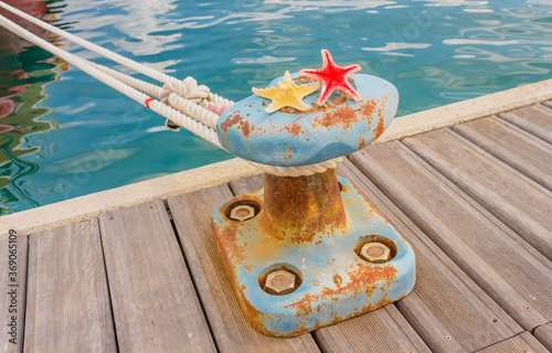 detail of a bitt with two starfishes and a rope for mooring at the harbor/the bitt is a low cast-iron column in the shape of a mushroom to tie chains and mooring ropes