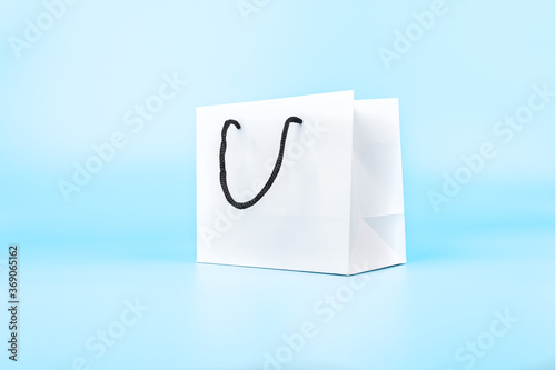 White paper shopping bag with black handle robe isolated on blue pastel background.