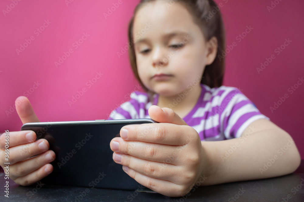 A smiling little girl watching an online video lesson on a smartphone at home, a Cute happy little child calling on a mobile phone with a teacher or tutor, home learning concept A smiling little girl watching an online video lesson on a smartphone at home, a Cute happy little child calling on a mobile phone with a teacher or tutor, home learning concept