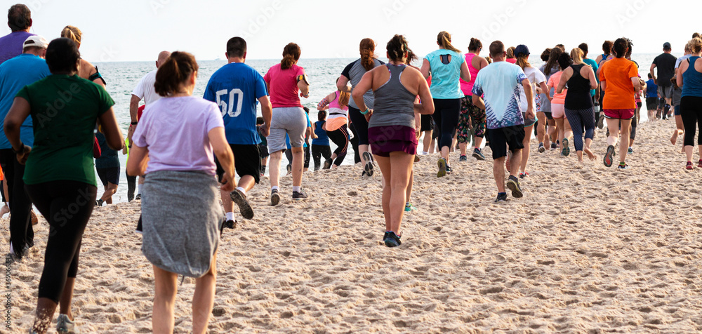 Obraz premium Rear view of adult runners running a one mile race on the beach