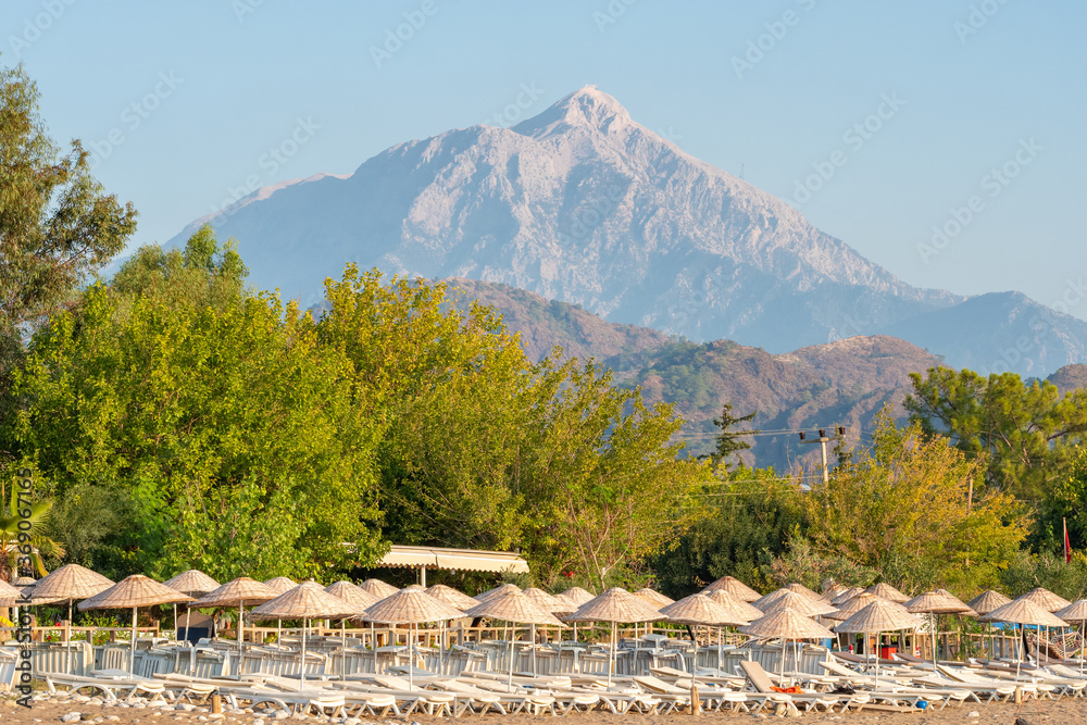 Beach umbrellas and sunbeds on the Cirali beach with Tahtali mountain at background in Turkey