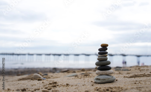 Canvas Print Pebble tower by the seaside with blurry pier down to the sea in Stack of zen rock stones on the sand, Stones pyramid on the beach symbolizing, stability, harmony, balance with shallow depth of field