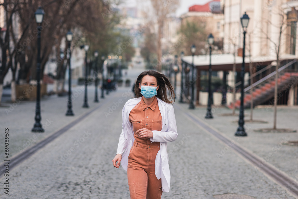 Obraz premium a brunette woman in orange clothes wearing white medical coat and a protective mask on her face