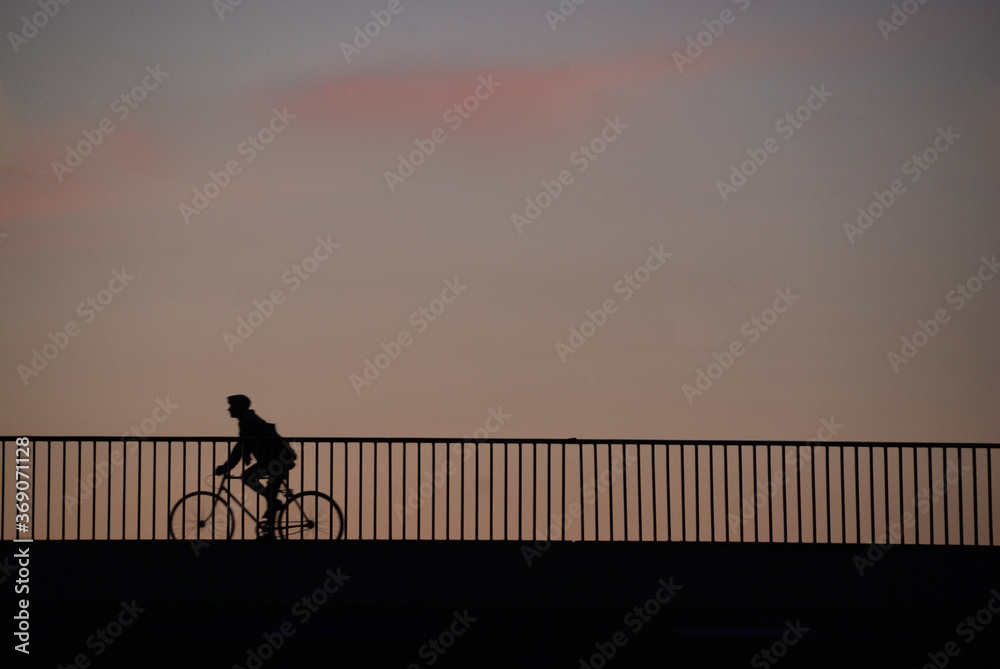 Silhouette of a man on a bicycle crossing a bridge at sunset – space behind him