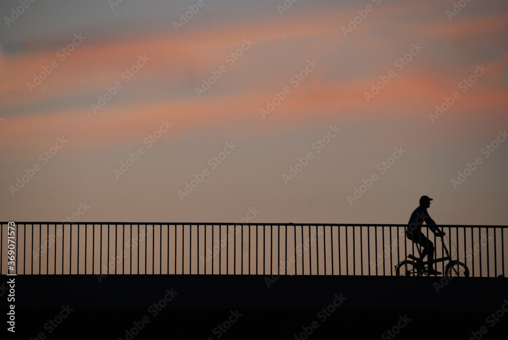Silhouette of a man on a small wheels bicycle crossing a bridge at sunset – space behind him